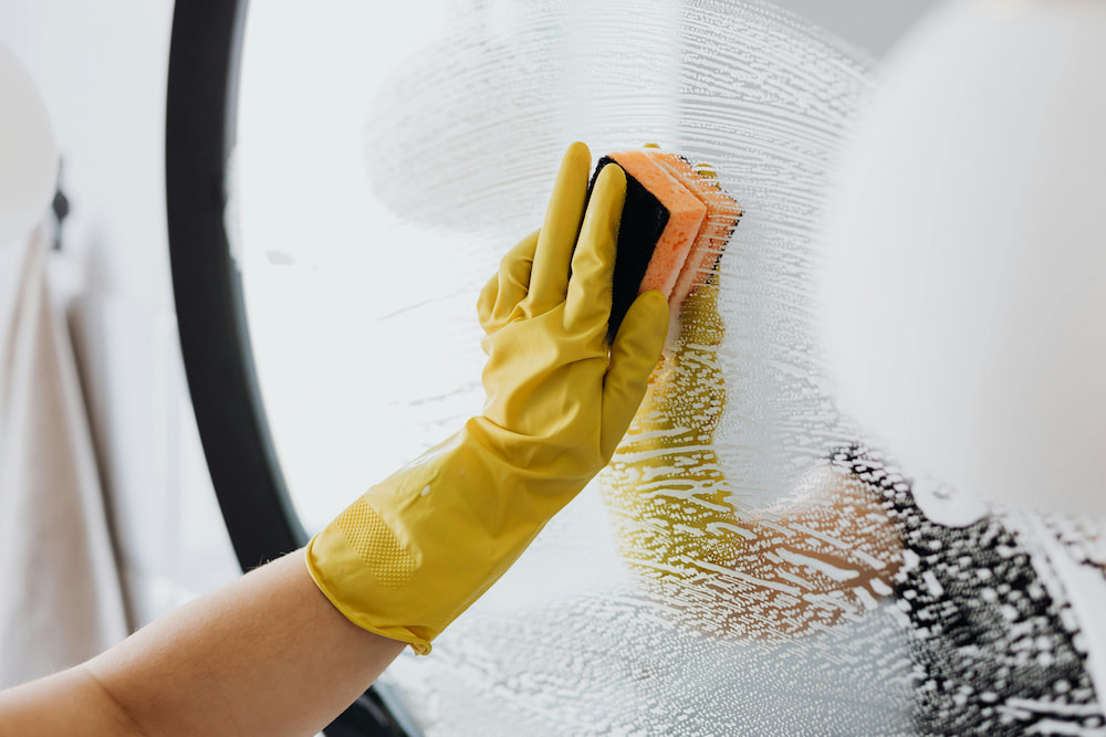 Human's Hand in yellow glove cleaning the glass of window